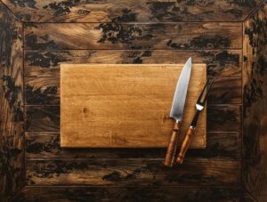 Träskärbräda med kockkniv och gaffel på mörkt träbord