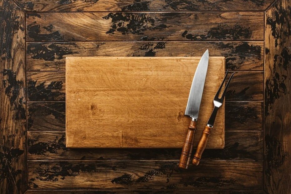 Träskärbräda med kockkniv och gaffel på mörkt träbord